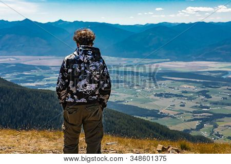Hiker Man Climbed On The Mountain Top. Guy Stands On The Mountain Hilltop. Scenic View To Kootenay V
