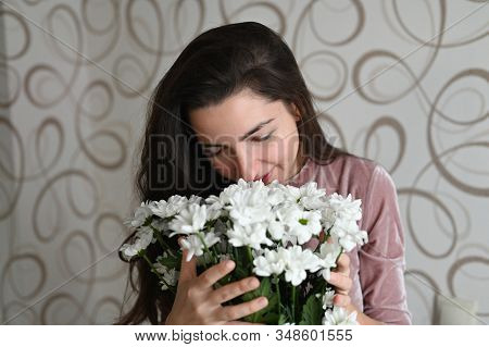 Girl Sniffs A Bouquet Of White Flowers. Brunette Hugs Sniffs A Bouquet Of Delicate Flowers From Her 