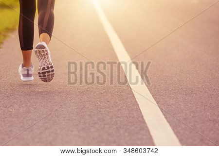 Close Up Sporty Woman Running On Road At Sunset. Fitness And Workout Wellness Concept.