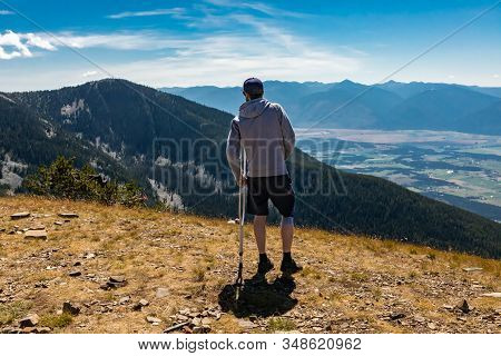 Unrecognizable Man Holding Crutches On Top Of The Mountain. View From Behind. Climbing To The Top. A