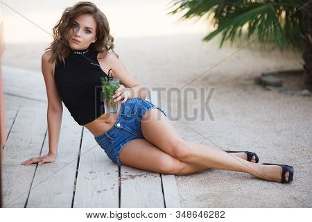 Beautiful Young Woman Enjoy Enjoys A Smoothie And Relax On Tropical Beach With Palm Tree. Summer Vac