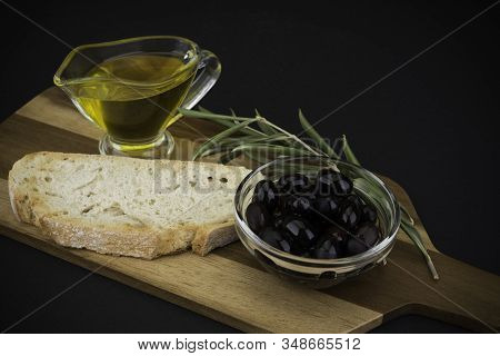 Olives With Olive Oil And Bread On Wooden Board. On Black Background.