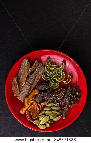 Top View Of Sliced Aloe Vera Pieces, Whole Spices, Cardamom, And Cloves In A Red Dish Plate On Black