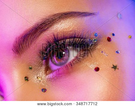 Colorful makeup. Bright and intense makeup. Female eye close-up with bright makeup. Fashionable stylish makeup with the use of sequins. Stylish image. The face is illuminated by bright lights.
