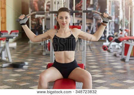 Indoor Shot Of Well Built Confident Good Looking Woman With Pony Tail Looking Directly At Camera, Si