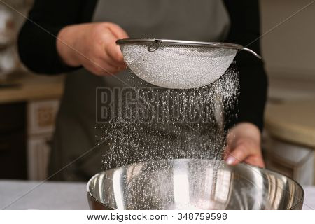 Female Cook In Apron Sifts Flour In A Metal Bowl. Preparing To Create A Dough For Baking Or Sculptin