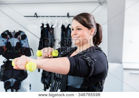 Big woman working on her fitness in wireless ems gym with weights