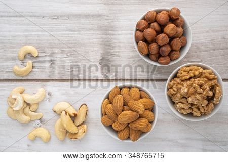 Different Nuts In White Bowls On Wood Table