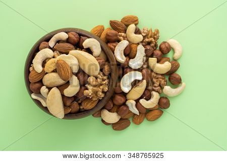 Different Nuts In Wooden Bowl On Green Background