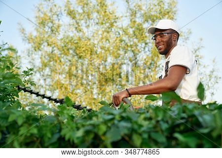 African Male Gardener Wearing Overalls With Protective Glasses Working With Professional Garden Equi