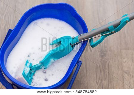 The Blue Bucket Of The Janitor Cleaner Is On The Floor Filled With Water And Detergent. Mop With A H