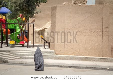Shape Of A Woman Walking In The Streets Of Yazd, Iran, Passing Near A Children Playground, Wearing A