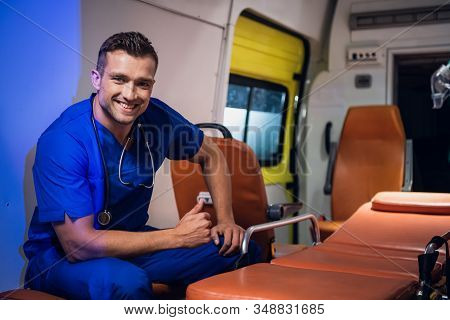 Young Corpsman In Blue Medical Uniform Sits In The Ambulance Car And Smiles