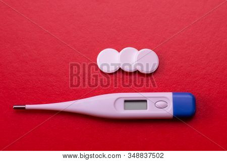Electronic Thermometer And Pills On A Red Background. Means For Treating Flu And Colds, Lowering The