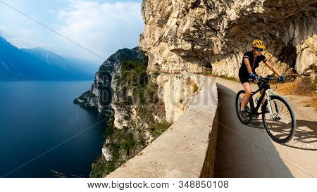 Cycling woman riding on bike at sunrise mountains and Garda lake landscape. Cycling MTB enduro flow sentiero ponale trail track. Outdoor sport activity.