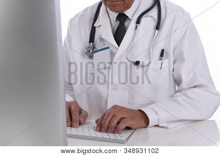 Closeup of a docor partially behind his computer screen as he types on his keyboard. Man is unrecognizable. 