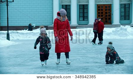 A Young Woman Mother Skating On Ice With Her Children - Hepling Them Get Up From The Ice