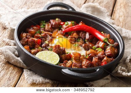 Sizzling Spicy Pork Sisig With Egg Ang Lime Close-up In A Pan. Horizontal