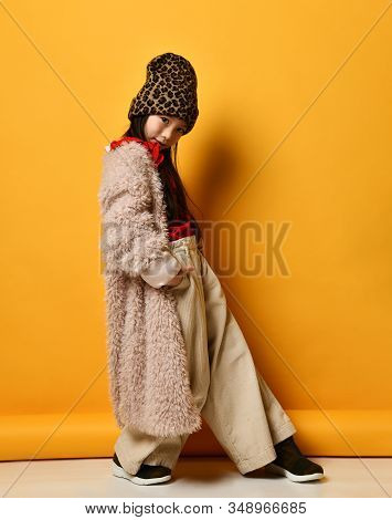 Little Asian Child In Red Blouse, Hat With Leopard Print, Beige Pants And Faux Fur Coat, Brown Boots