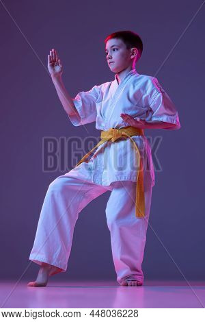 Studio Shot Of Sportive Kid, Male Taekwondo, Karate Athletes In Doboks Posing Isolated On Purple Bac