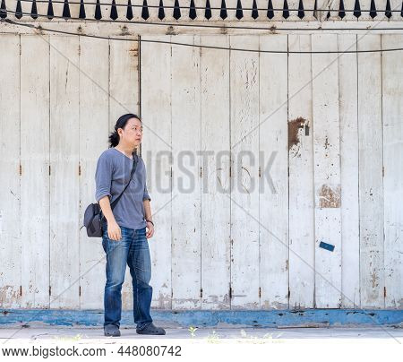 Asian Long Hair Man Is Standing And Posting In Front Of The Old White And Blue Wood Wall On Foot Pat