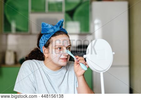 Happy Woman Applying Moisturizing Mask On Face For Skin Care With Special Rubber Brush Wearing Blue 