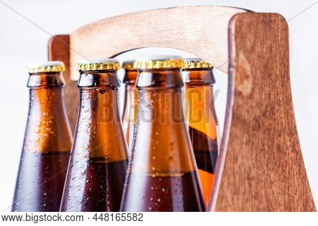 Close-up Of Wet Six Bottles Necks Of Beer In A Wooden Case On A White Background. Alcoholic Drinks F