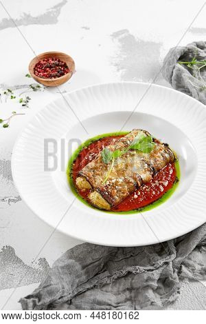 Eggplant rolls stuffed with tomato and cheese. Baked eggplant and cheese rollatini. Eggplant appetizer in white plate on stone background. Plant-based menu