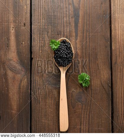 Fresh Grainy Black Paddlefish Caviar In Brown Wooden Spoon On A Black Background, Top View