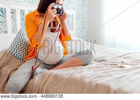 Pregnant Woman Holding Retro Photocamera On Bed. Pregnant Girl Making Photos.
