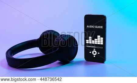 Audio Guide Online App On Digital Mobile Smartphone Screen With Music Headphones On Neon Background.