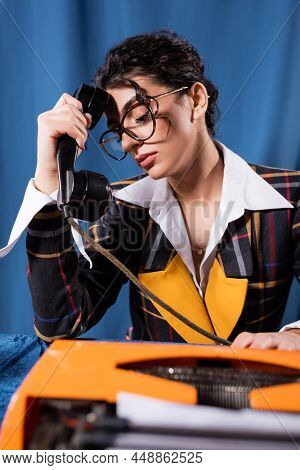 Tired Newswoman Sitting With Handset Near Typewriter On Blue Background