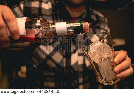 Hands Of Bartender Pouring Red Liqueur Into Glass With Ice