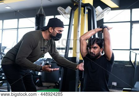 Focus On Gym Trainer With Medical Face Teaching Or Training To Lift Dumbells At Fitness Center Durin