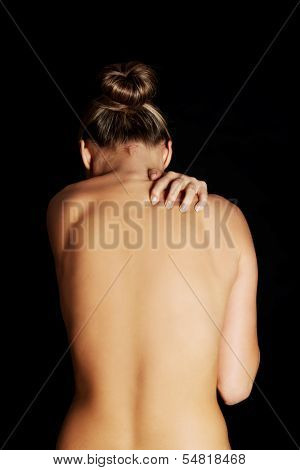 Nude, topless woman, scratching her neck. back view. On black background. 
