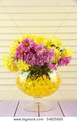 Beautiful flowers in vase with hydrogel on table on wooden background