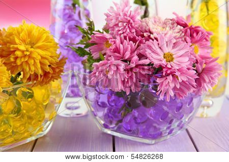 Beautiful flowers in vases with hydrogel on table close up