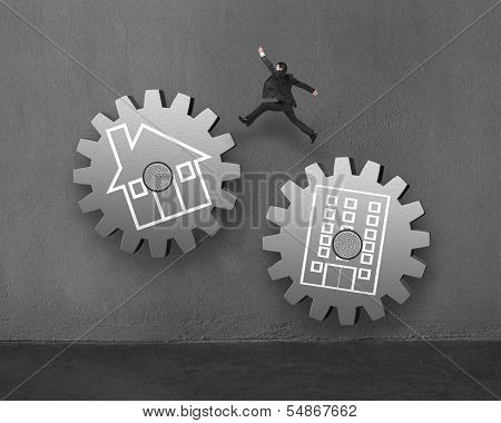 Businessman Jumping On Large Concret Gear, From Office To Home