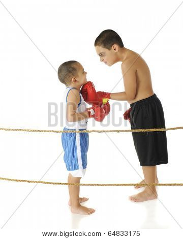 A tough-acting elementary boxer with a shiner threatening his preschool brother while standing behind boxing ring ropes.  On a white background.