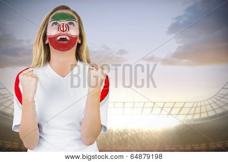 Excited iran fan in face paint cheering against large football stadium under cloudy blue sky