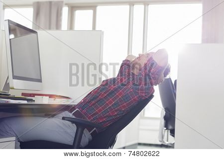 Side view of young businessman relaxing at computer desk in office