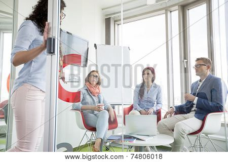 Business people looking at female colleague standing in sliding door