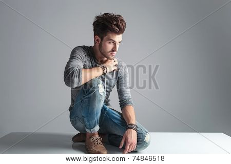 Attractive fashion man looking away from the camera while relaxing on the floor, on grey studion background.