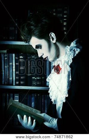 Handsome vampire nobleman studying ancient books in the library. Halloween. Dracula costume.