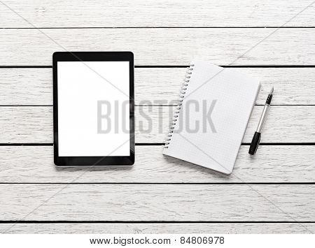 Tablet computer with notepad on white wooden desk. Clipping path included.