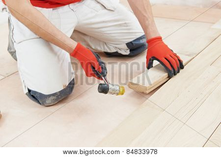 carpenter worker installing wood parquet board during flooring work with hammer