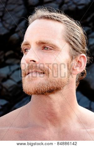 Charismatic attractive shirtless blond man with a beard and moustache staring thoughtfully to the side with a quiet smile and faraway dreamy expression