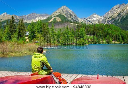 Young man at pier mountain lake with high peaks