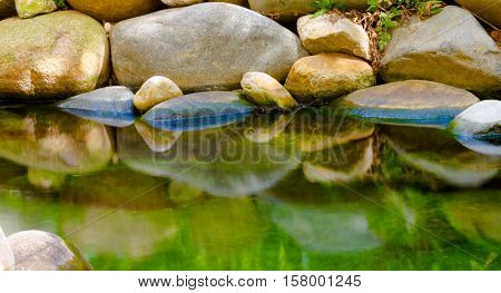 Calm Small lake with rocks on the shore reflecting on cristal water