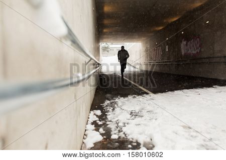 fitness, sport, people, season and healthy lifestyle concept - young man running along pedestrian subway tunnel in winter